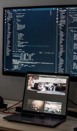 A larger computer screen with a laptop in front of it, displaying coding and website components